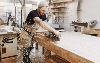 Carpenter Working With Electric Planer On Wooden Plank In Workshop. Craftsman Makes Own Successful Small Business.